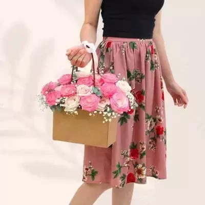 Woman holding a floral arrangement in a box with pink and cream roses.