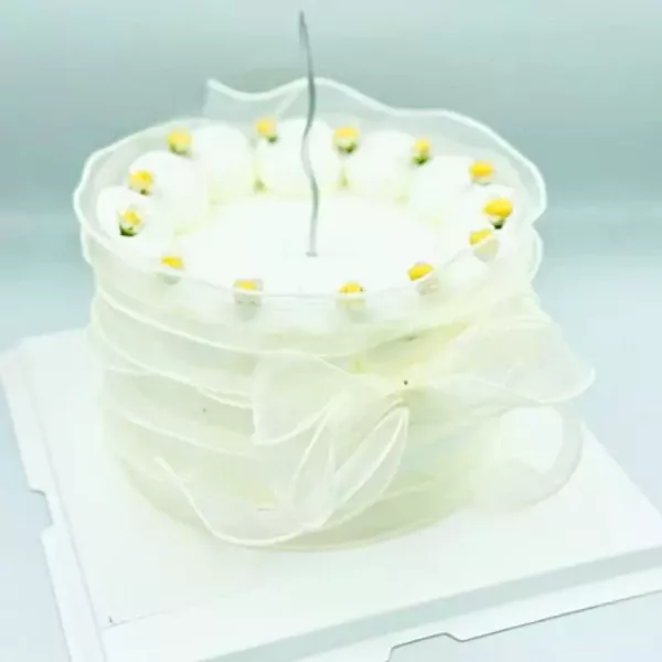 Delicate white cake with sheer ruffled trim and tiny yellow-topped white flowers.