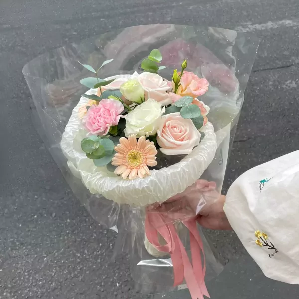 Bouquet of pink and cream roses, carnations, gerberas, and eucalyptus in cellophane with pink ribbon.