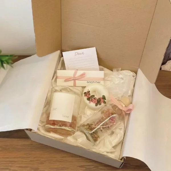 A gift box with a candle, glass jar of dried flowers, and a note.