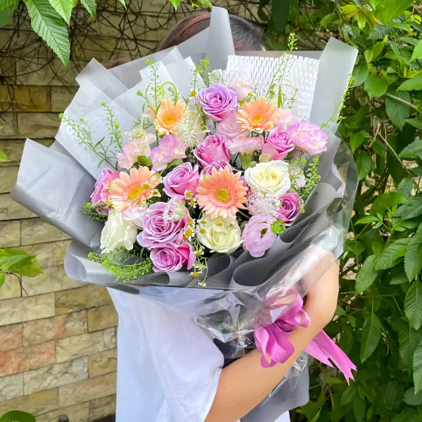A lush bouquet of pink, purple, and white roses, gerbera daisies, and carnations.