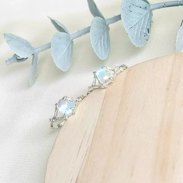 Silver ring with two moonstones in a delicate branch design, resting on wood.