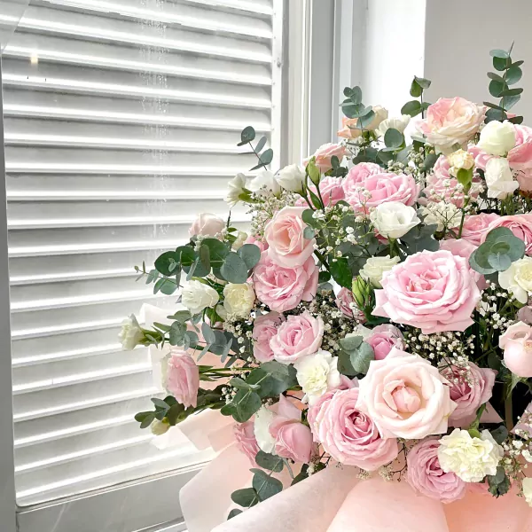 A bouquet of pink and white roses with greenery, against a white louvered background.