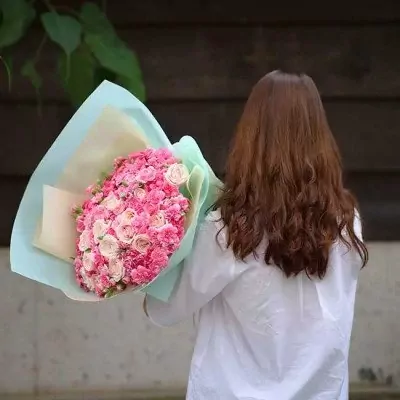 Woman holding a large bouquet of pink and white roses and carnations.