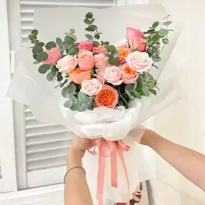 Pink and orange roses with eucalyptus, wrapped in white paper with a pink ribbon.