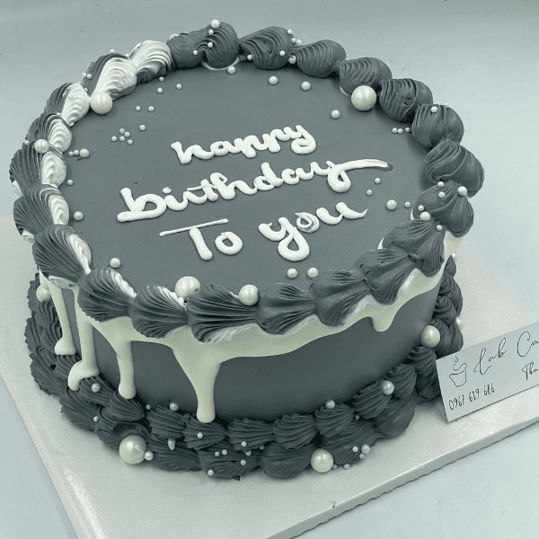Dark gray birthday cake with white lettering and frosting decorations.