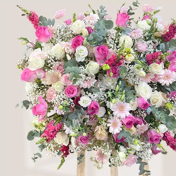 A large floral arrangement in shades of pink and white, featuring roses, carnations, and baby's breath.