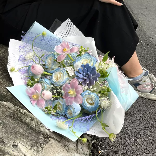 Bouquet of blue and pink roses with tulips and succulents in light blue wrapping.