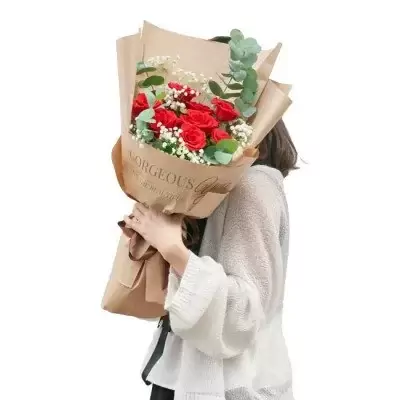 A bouquet of red roses and baby's breath wrapped in kraft paper with "Gorgeous You" printed on it.