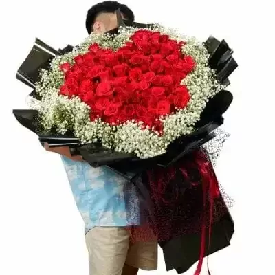 A person hugging a large bouquet of 101 red roses with baby's breath.