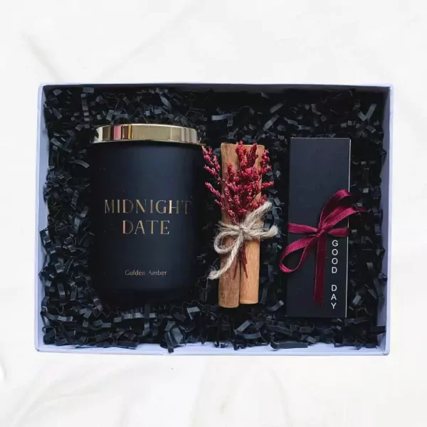 Gift set with a black candle, cinnamon sticks, dried flowers, and a black box with a red ribbon.