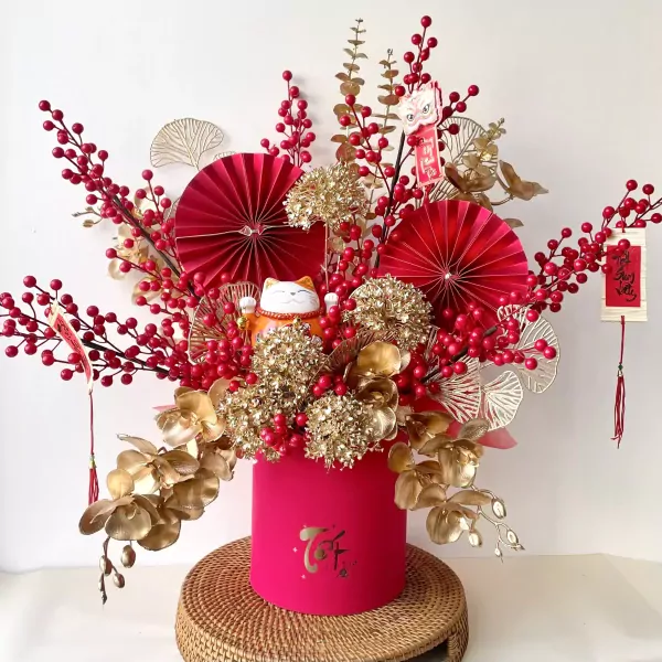 Red and gold floral arrangement with a lucky cat, red berries, fans, and orchids in a pink box.