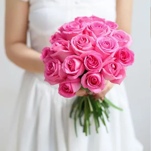 Bride in white dress holding a bouquet of 20 pink roses.