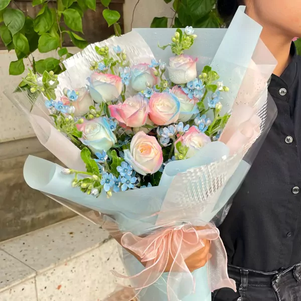 Rainbow dyed roses and blue flowers bouquet with a pink ribbon tied around the stems.
