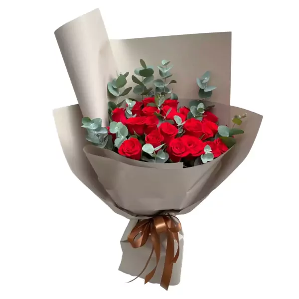 Bouquet of red roses and eucalyptus leaves wrapped in taupe paper with a brown ribbon.