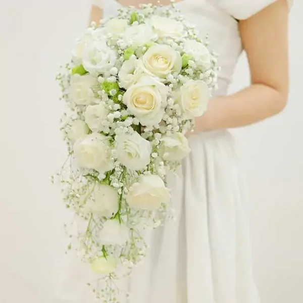A bride in a white dress holding a cascading bouquet of white roses and baby's breath.