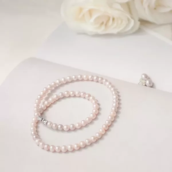 Pearlie Pearl Necklace with delicate pink pearls and a silver clasp, styled with white roses.