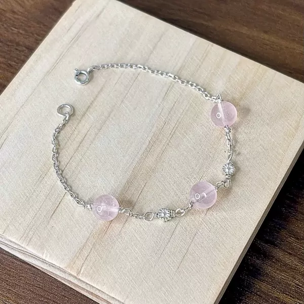 Silver bracelet with pink beads and small flower charms on a wooden surface.