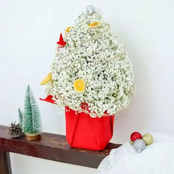 A white baby's breath Christmas tree in a red pot with dried orange slices and a gnome.