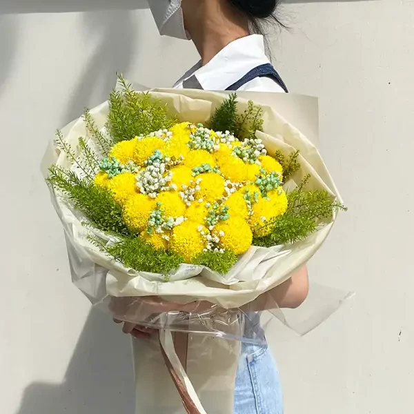 A person holds a bouquet of yellow ping pong chrysanthemums, baby's breath, and greenery.
