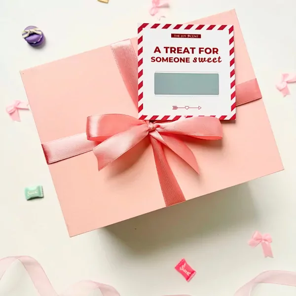 Pink gift box with a red and white tag that says "A treat for someone sweet," surrounded by ribbons and candy accents.