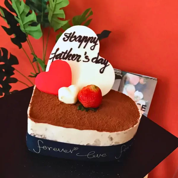 Heart-shaped Tiramisu cake with "Happy Father's Day" topper, strawberry, and red heart decoration.
