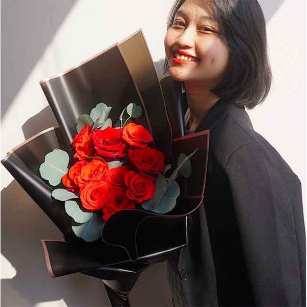 Woman smiling holding a bouquet of red roses in black wrapping.