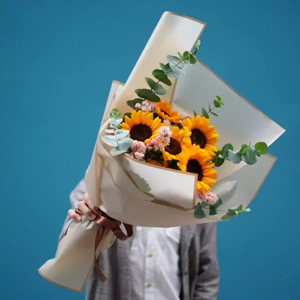 Bouquet of sunflowers and eucalyptus, held by a person in a white shirt and grey cardigan.