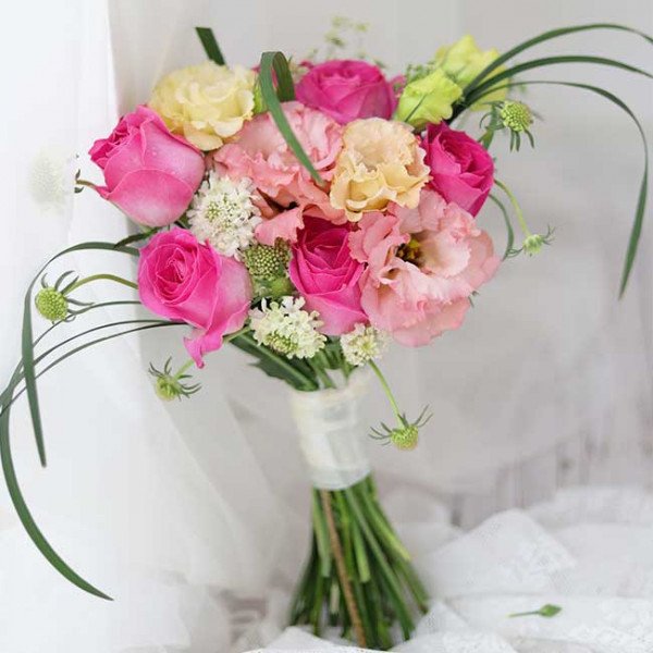 Pink and yellow wedding bouquet with roses, lisianthus, and greenery.